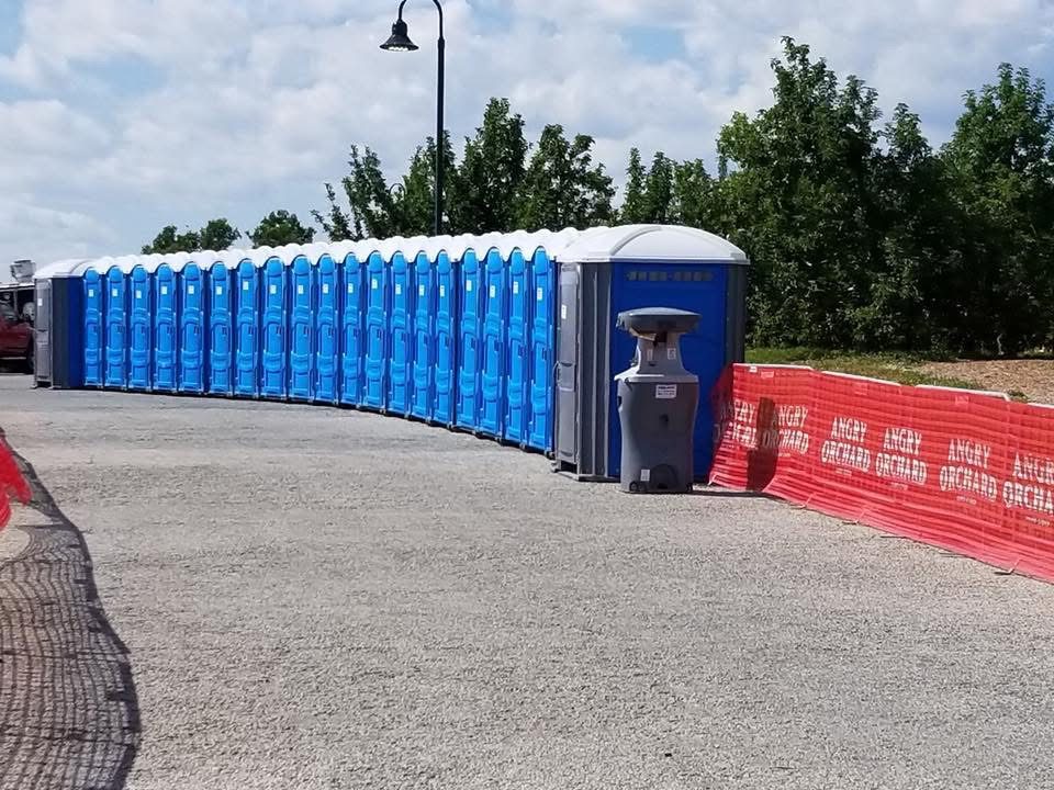 Row of blue portable toilets lined up outdoors with a single gray unit at the front.